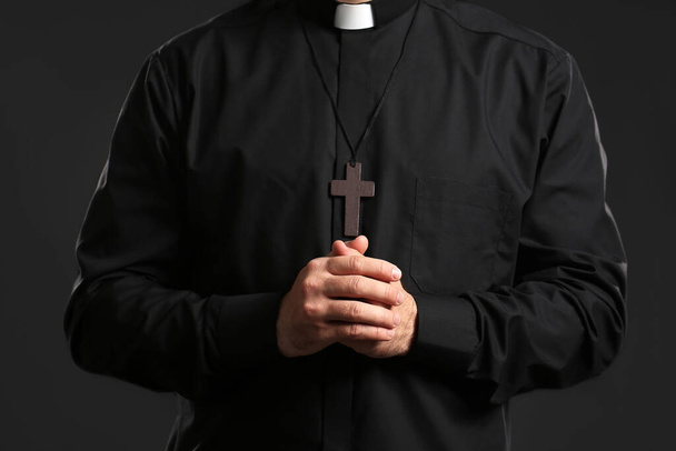 Young priest praying to God on dark background - Foto, afbeelding