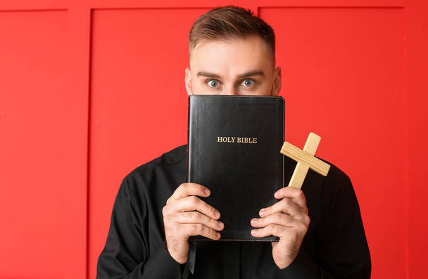 Junger Priester mit Bibel auf farbigem Hintergrund - Foto, Bild