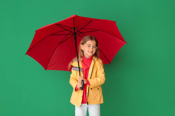 Yağmurluk giymiş şirin bir kız ve arka planda şemsiyesi var. - Fotoğraf, Görsel