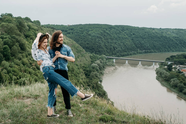 Joven pareja viajera de moda divirtiéndose en la cima de la colina disfrutando de la puesta de sol sobre el valle cerca del río, viajes y senderismo Concepto de viaje
 - Foto, imagen
