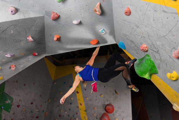 Rock climber woman hanging on a bouldering climbing wall, inside on colored hooks - Foto, Imagem