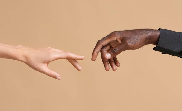 Руки кавказької жінки і афро-американського чоловіка тягнуться один до одного на кольоровому тлі. Концепція расизму - Фото, зображення