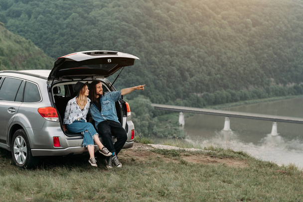 Junge stylische reisende Hipster mit Spaß im Kofferraum in der Nähe des River Canyon Reise- und Roadtrip-Konzepts - Foto, Bild