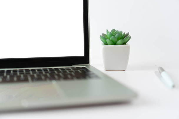 Ноутбук з білим порожнім екраном ізольований на білому тлі з маленькою рослиною і прикрашений гаджетом на робочому столі
. - Фото, зображення