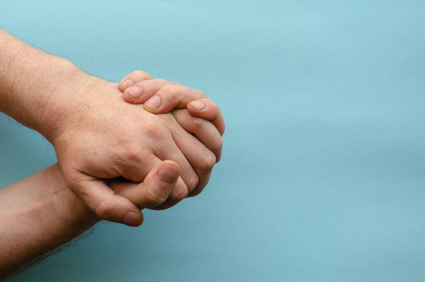 Két férfi kéz összekapcsolt ujjai kék háttérrel. Egy kaukázusi etnikumú felnőtt keze. Kézmozdulatok sorozata. Kilátás fentről. Másold a helyet. Szelektív fókusz. - Fotó, kép