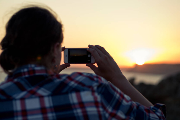 Nainen, joka ottaa kuvia iphonella auringonlaskun aikana merellä näköalapaikalla Ponta da Piedadessa Lagosissa, Portugalissa. - Valokuva, kuva