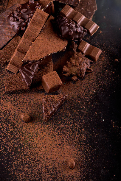 Broken chocolate pieces and cocoa powder on wooden background - Foto, afbeelding