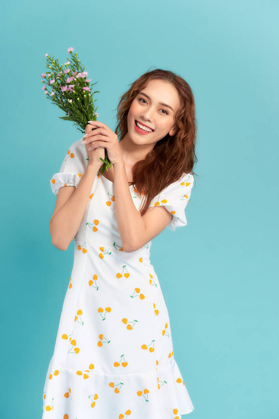 Прекрасная молодая женщина, держащая букет цветов и улыбаясь, стоя изолированно на синем фоне - Фото, изображение