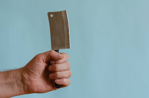 La mano de un macho adulto sostiene un pequeño hacha de cocina. Un pequeño cuchillo con una empuñadura negra en la mano izquierda. Hombre de mediana edad de raza europea. Cubertería
. - Foto, Imagen