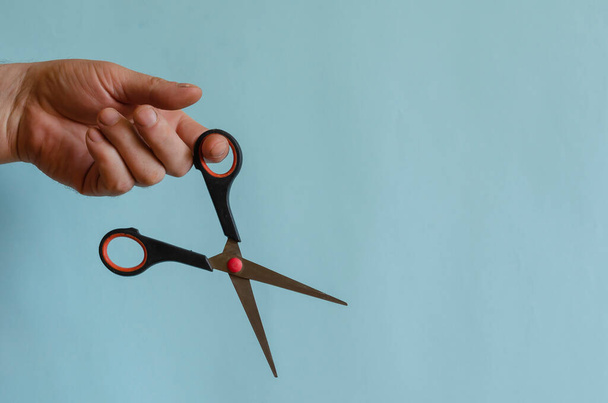 Sharp scissors with black and red arms in a male hand. Small stationery scissors in the left hand. Middle-aged man of European race. Stationery - Фото, изображение