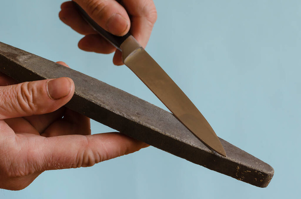 De handen van de man slijpen een klein mes op een slijpsteen. Het proces van handmatig slijpen van een snijgereedschap. Man van middelbare leeftijd van Europees ras. Handgereedschap - Foto, afbeelding