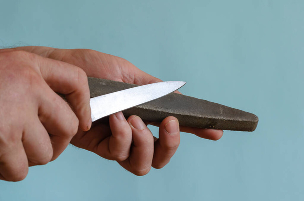 Les mains de l'homme aiguisent un petit couteau sur une meule. Le processus de broyage manuel d'un outil de coupe. Homme d'âge moyen de race européenne. Outil à main - Photo, image