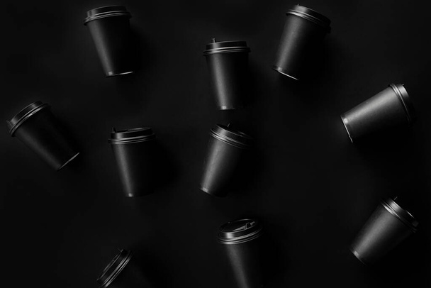 Scattered black paper cups close up on a black background. Recycling craft paper cups of coffee to go. Selective focus. Craft cup for hot beverage, takeaway. Disposable cup. Minimalist Style - Foto, immagini