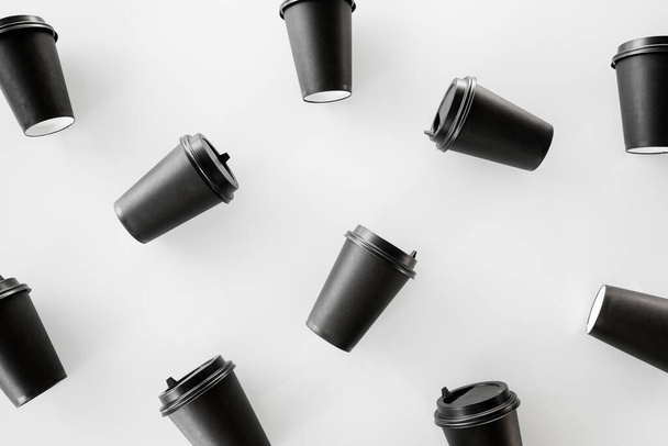 Rozrzucone czarne kubki papierowe zamykają się na białym tle. Recykling kubki papierowej kawy na wynos. Wybiórcze skupienie. Kubek na gorący napój, na wynos. Jednorazowy kubek. Styl minimalistyczny - Zdjęcie, obraz