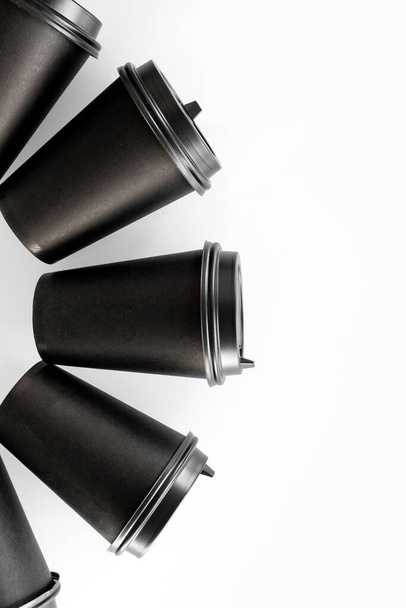 Pattern of black paper cups for tea or coffee on a white background. Recycling craft paper cups of coffee to go. Selective focus. Craft cup for hot beverage, takeaway. Disposable cup. Minimalist Style - Photo, Image