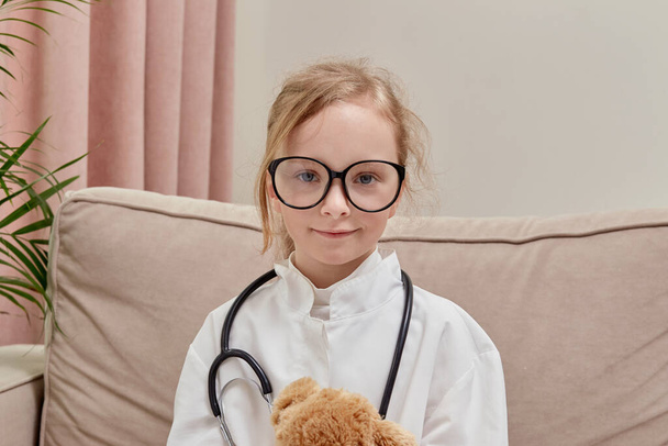 The game of the doctor. A girl in doctor clothes and glasses looks at the camera - Foto, imagen