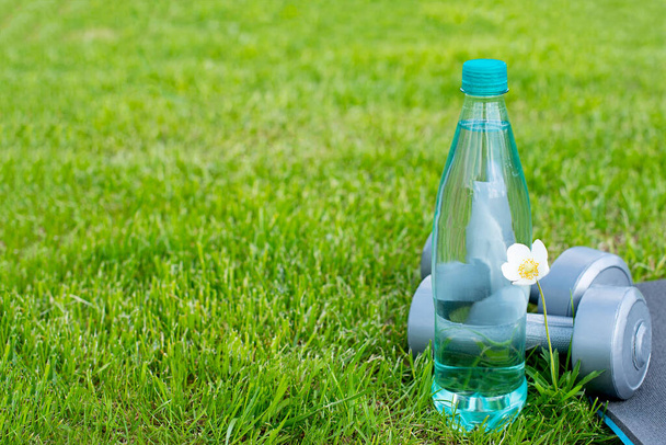Botella con agua, pesas y una esterilla para deportes y yoga en la hierba verde. Copiar espacio
. - Foto, imagen