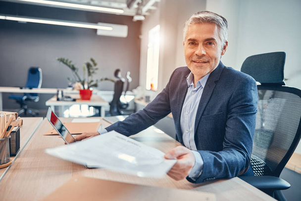Entrepreneur of company sitting on the chair at his desk and giving a document - Foto, Imagen