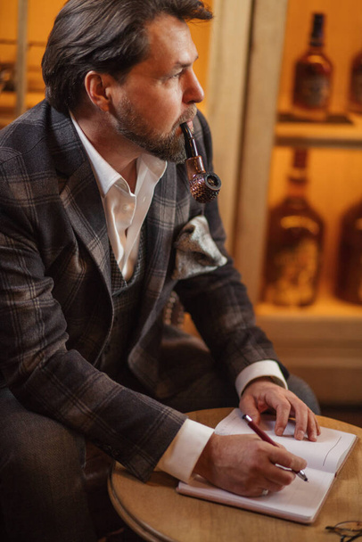 Mature businessman smoking tobacco pipe and making notes, working at his office. - Foto, Bild