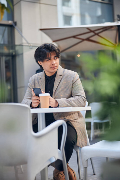 Handsome young man using mobile phone in outdoor cafe - Фото, изображение