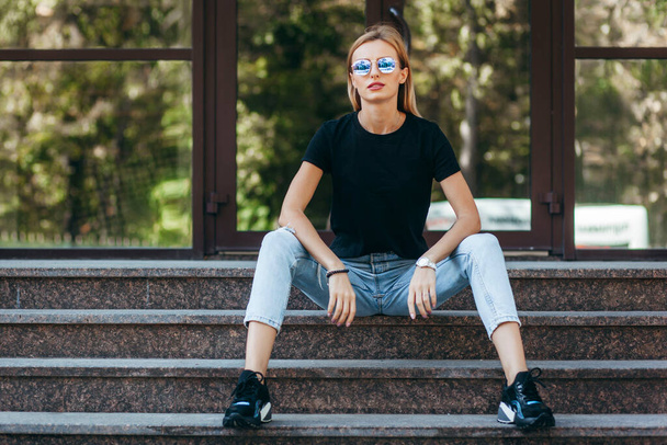 Stylish blonde girl wearing black t-shirt and glasses posing against street , urban clothing style. Street photography - Fotoğraf, Görsel