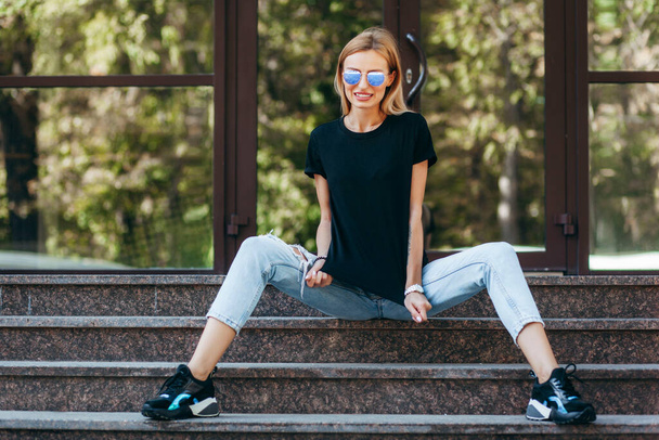 Stilvolles blondes Mädchen mit schwarzem T-Shirt und Brille, das gegen den Stil urbaner Straßenkleidung posiert. Straßenfotografie - Foto, Bild