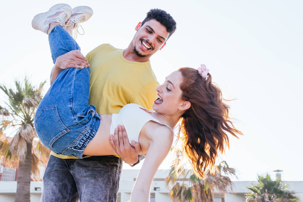 jonge man draagt zijn vriendin terwijl glimlachen in de zomer - Foto, afbeelding