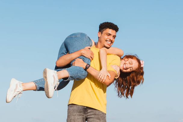 junger Mann trägt seine Freundin lächelnd auf dem Rücken - Foto, Bild