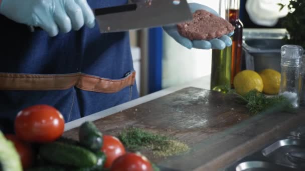 professional chef with gloves cook makes meat medallions for hamburgers with meat knife on cutting board background of vegetables, local producer - Footage, Video