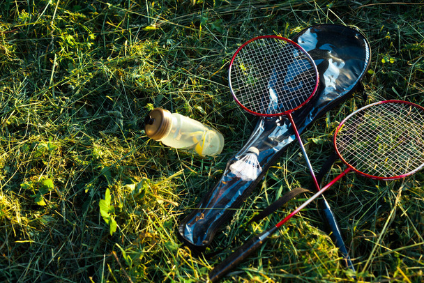 Бадмінтонні ракетки з пляшкою води на траві
 - Фото, зображення