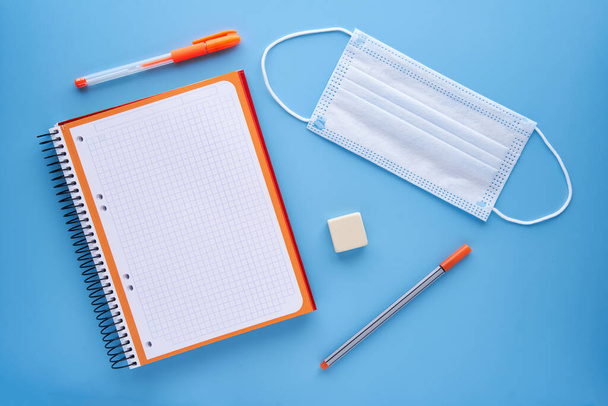 Notebook and pen with a mask on a blue background. Back to school concept and protection against covid. - Photo, Image