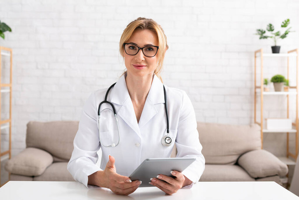 Contato com pacientes online. Mulher médica com óculos e casaco branco segura tablet digital nas mãos
 - Foto, Imagem