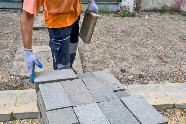 De meester legt nieuwe betonnen bakstenen voor de stoep op de stapel. De stenen zijn klaar voor de aanleg van een nieuw voetpad.. - Foto, afbeelding