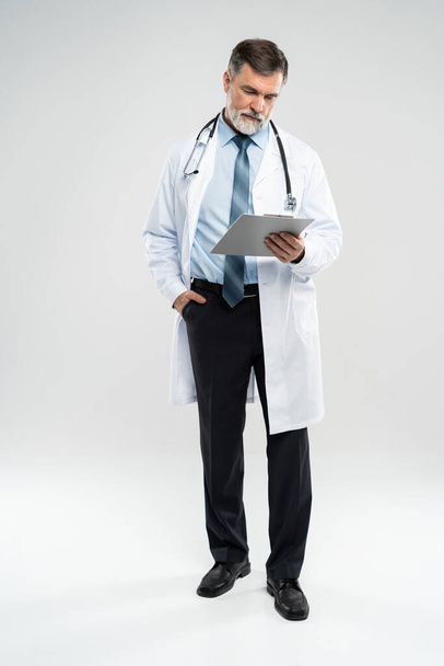 full body picture of a mature doctor holding a notepad, on white background. - Fotoğraf, Görsel