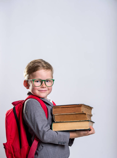 Boldog iskolás fiú hátizsákkal és fehér hátterű könyvekkel. Vissza az iskolába - Fotó, kép