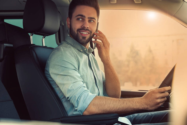 Handsome young man talking on smartphone while driving his car - Fotoğraf, Görsel