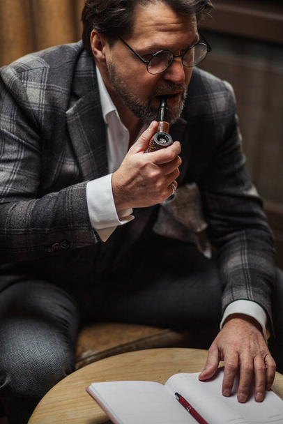 Mature businessman smoking tobacco pipe and making notes, working at his office. - Fotó, kép
