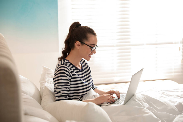 Young woman working with laptop on bed at home - Foto, Bild