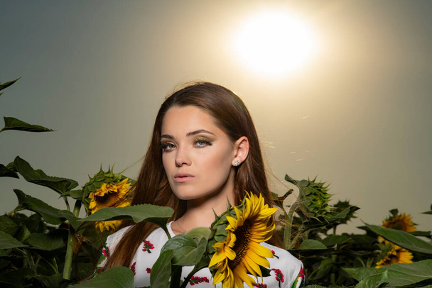 Schöne junge Mädchen posiert bei Sonnenuntergang in einem Sonnenblumenfeld - Foto, Bild