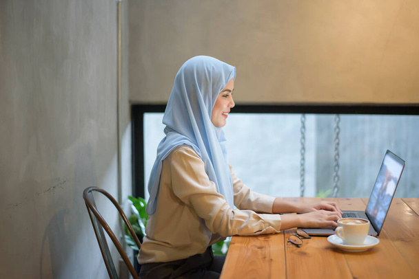Muslim woman with hijab is working with laptop computer in coffee shop - Фото, зображення