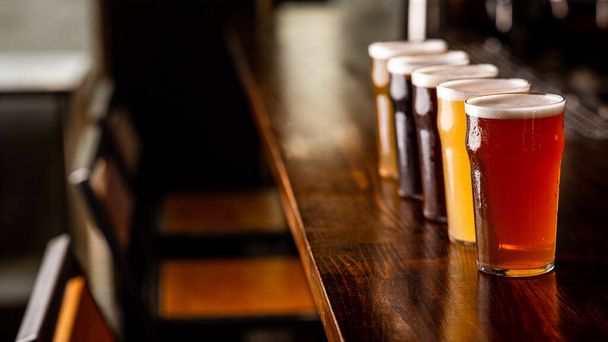 Fête avec des amis au pub. Rangée de verres de bière de différentes sortes sur le comptoir du bar à l'intérieur - Photo, image