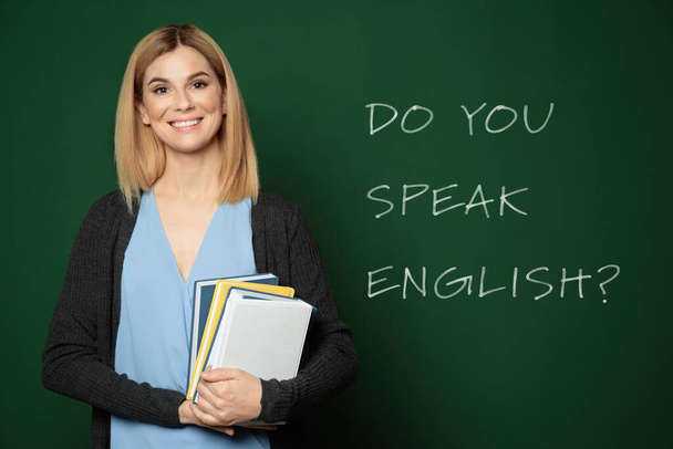 Beautiful teacher near green chalkboard with text Do You Speak English - Foto, Bild