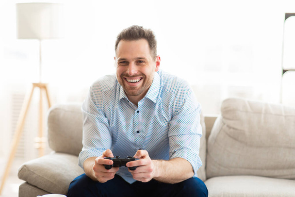 Young man sitting on couch playing video games online - Fotografie, Obrázek