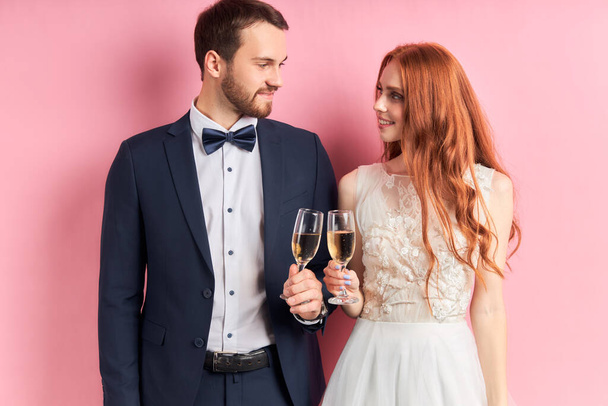 Lovely couple wearing white dress and tuxedo holding glass of champagne - Foto, Imagem