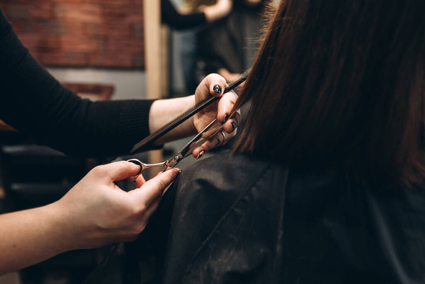 Meester kapper knipt een meisje haar haar met een schaar - Foto, afbeelding