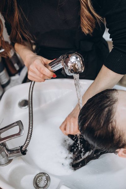 Hairdresser washes the hair of a brunette client - 写真・画像