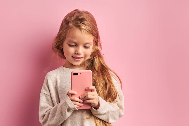 Portrait of charming cute sweet girl with smartphone in hands isolated on pink background - Foto, Bild