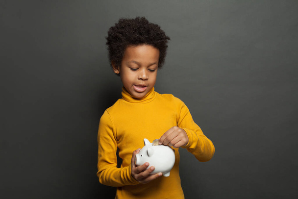 Cute black child putting in piggy bank euro coin - Фото, зображення
