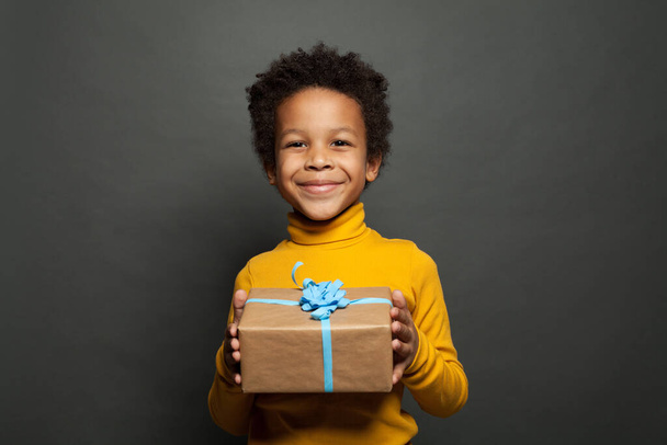 Μικρό μαύρο παιδί αγόρι χαμογελά και κρατώντας δώρο σε μαύρο φόντο - Φωτογραφία, εικόνα