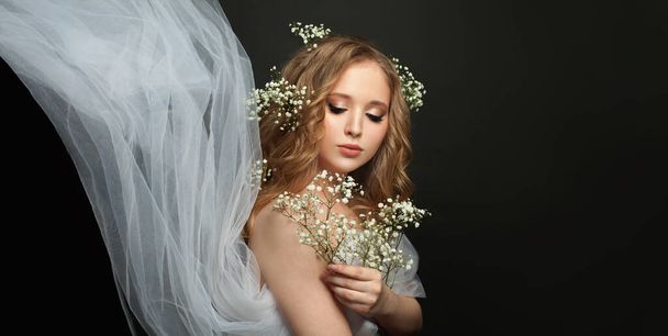 Νεαρή γυναίκα που κρατά λευκά λουλούδια σε μαύρο φόντο - Φωτογραφία, εικόνα